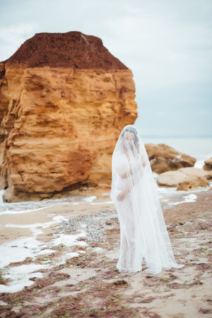 bride in her underwear and a dressing gown with a veil walks on the beachの写真素材