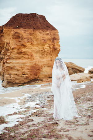 bride in her underwear and a dressing gown with a veil walks on the beachの写真素材