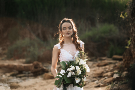 Bride with a wedding bouquet on the shore of the black sea in the sunset lightの写真素材
