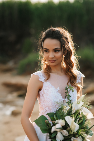 Bride with a wedding bouquet on the shore of the black sea in the sunset lightの写真素材