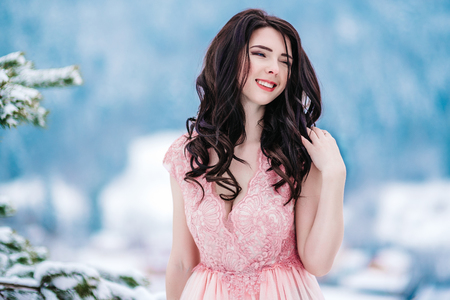girl with chestnut hair, blue eyes and a pink dress on the background of the winter mountainsの写真素材