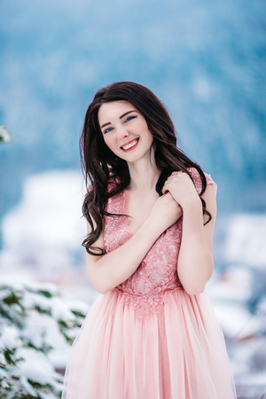 girl with chestnut hair, blue eyes and a pink dress on the background of the winter mountainsの写真素材
