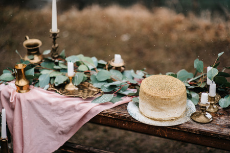 wedding decor with a golden cake on a wooden bench against a waterfall backgroundの写真素材