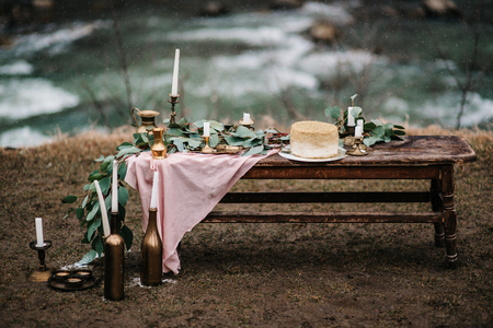 wedding decor with a golden cake on a wooden bench against a waterfall backgroundの写真素材