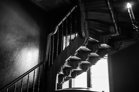 old antique spiral staircase leading upwards against the background of a glowing windowの写真素材