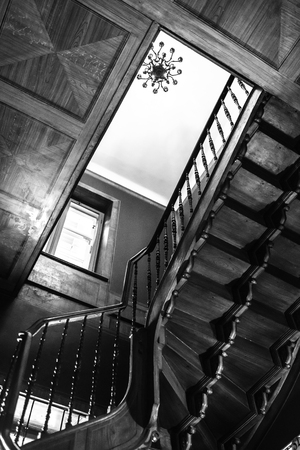 old antique spiral staircase leading upwards against the background of a glowing windowの写真素材