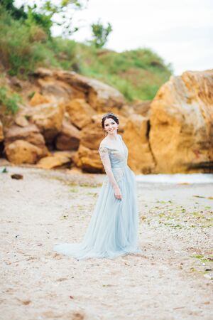 bride in a blue light dress walking along the oceanの写真素材