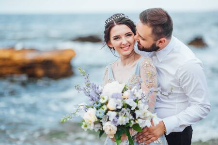 same couple with a bride in a blue dress walk along the ocean shoreの写真素材