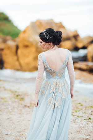 bride in a blue light dress walking along the oceanの写真素材