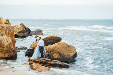 same couple with a bride in a blue dress walk along the ocean shoreの写真素材