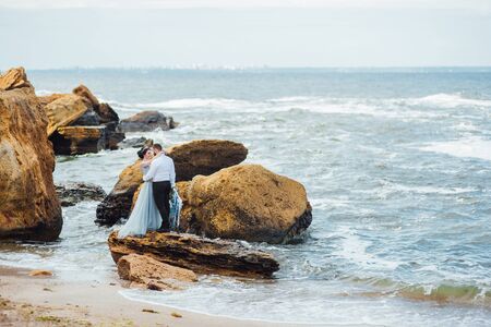same couple with a bride in a blue dress walk along the ocean shoreの写真素材