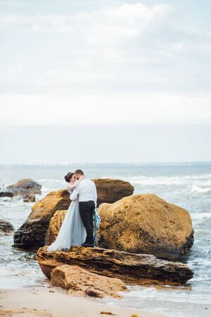 same couple with a bride in a blue dress walk along the ocean shoreの写真素材
