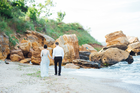 same couple with a bride in a blue dress walk along the ocean shoreの写真素材