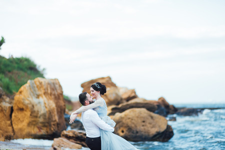 same couple with a bride in a blue dress walk along the ocean shoreの写真素材