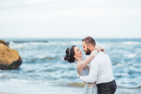 same couple with a bride in a blue dress walk along the ocean shoreの写真素材