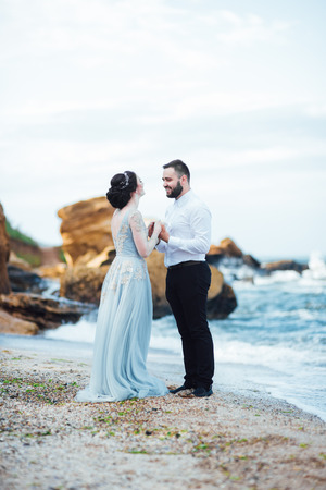 same couple with a bride in a blue dress walk along the ocean shoreの写真素材