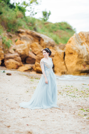 bride in a blue light dress walking along the oceanの写真素材