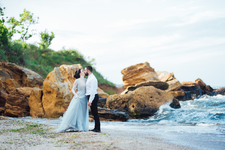 same couple with a bride in a blue dress walk along the ocean shoreの写真素材