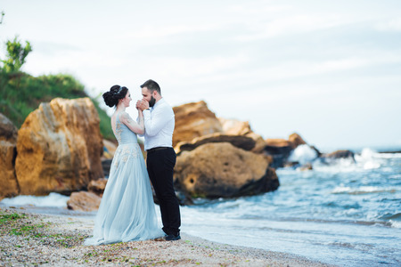 same couple with a bride in a blue dress walk along the ocean shoreの写真素材