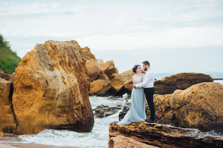same couple with a bride in a blue dress walk along the ocean shoreの写真素材