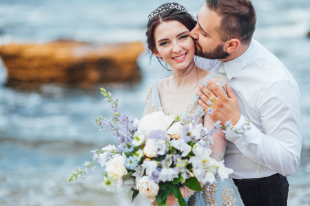 same couple with a bride in a blue dress walk along the ocean shoreの写真素材