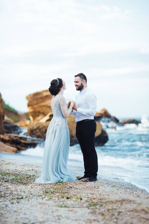 same couple with a bride in a blue dress walk along the ocean shoreの写真素材