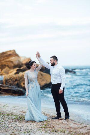 same couple with a bride in a blue dress walk along the ocean shoreの写真素材