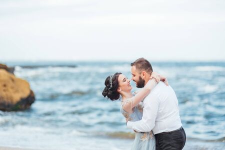 same couple with a bride in a blue dress walk along the ocean shoreの写真素材