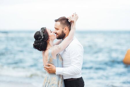 same couple with a bride in a blue dress walk along the ocean shoreの写真素材