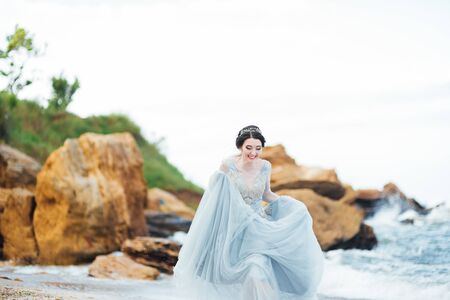 bride in a blue light dress walking along the oceanの写真素材