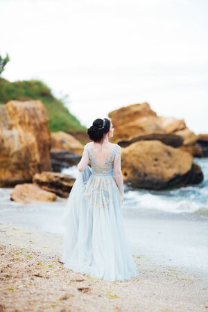bride in a blue light dress walking along the oceanの写真素材