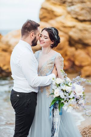 same couple with a bride in a blue dress walk along the ocean shoreの写真素材