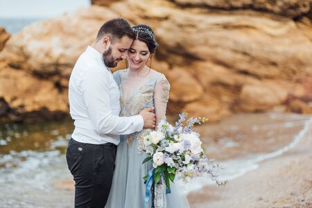 same couple with a bride in a blue dress walk along the ocean shoreの写真素材
