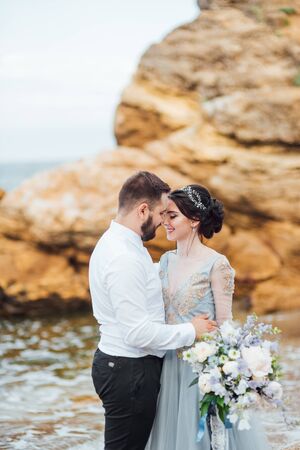 same couple with a bride in a blue dress walk along the ocean shoreの写真素材