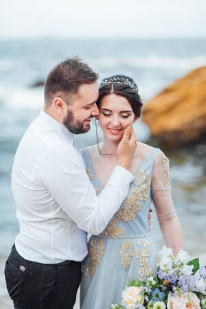 same couple with a bride in a blue dress walk along the ocean shoreの写真素材
