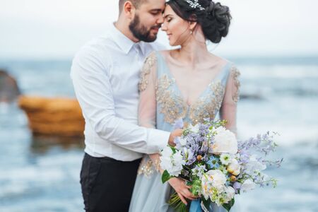 same couple with a bride in a blue dress walk along the ocean shoreの写真素材