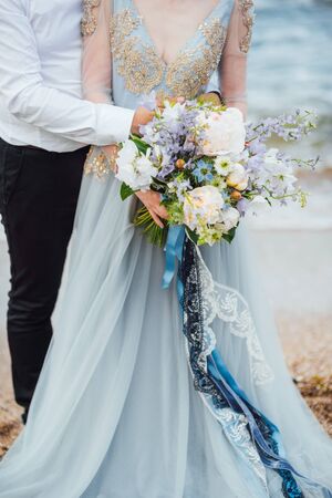 same couple with a bride in a blue dress walk along the ocean shoreの写真素材
