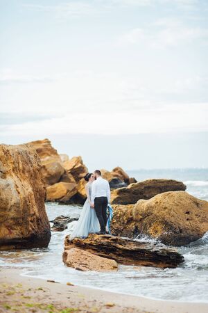 same couple with a bride in a blue dress walk along the ocean shoreの写真素材