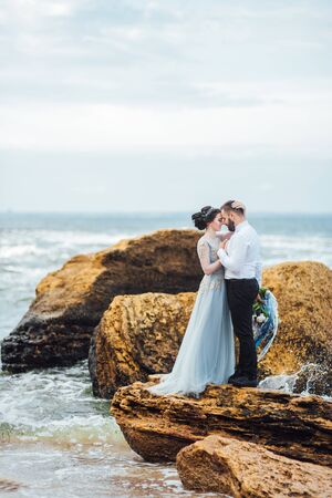 same couple with a bride in a blue dress walk along the ocean shoreの写真素材