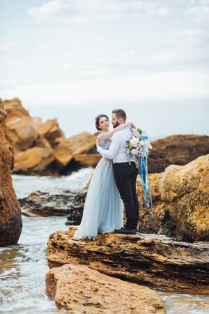 same couple with a bride in a blue dress walk along the ocean shoreの写真素材
