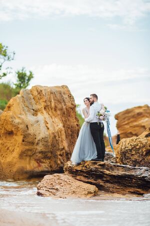 same couple with a bride in a blue dress walk along the ocean shoreの写真素材
