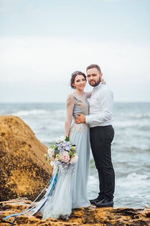 same couple with a bride in a blue dress walk along the ocean shoreの写真素材