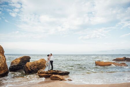 same couple with a bride in a blue dress walk along the ocean shoreの写真素材
