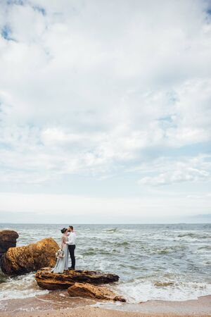 same couple with a bride in a blue dress walk along the ocean shoreの写真素材