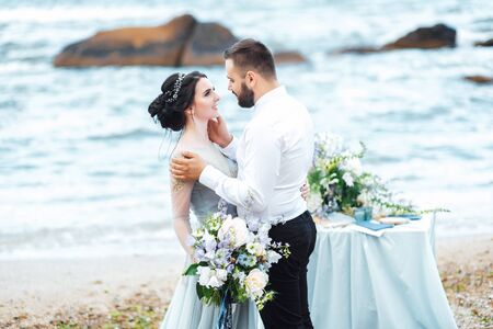 same couple with a bride in a blue dress walk along the ocean shoreの写真素材