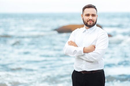 the groom in a white shirt and black pants stands on the beachの写真素材