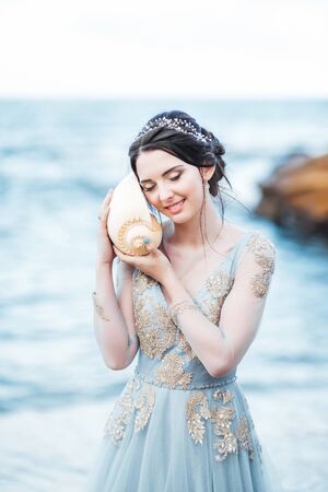 bride with a big shell on the beach in a blue wedding dressの写真素材