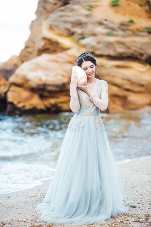 bride with a big shell on the beach in a blue wedding dressの写真素材