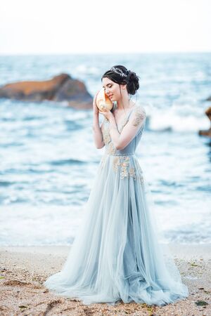 bride with a big shell on the beach in a blue wedding dressの写真素材