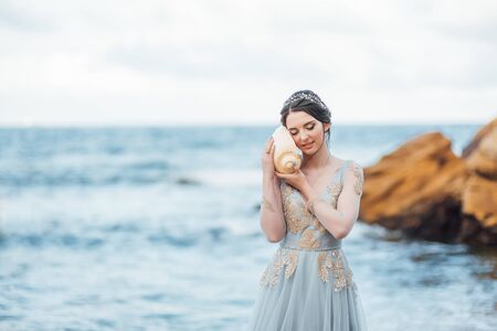 bride with a big shell on the beach in a blue wedding dressの写真素材